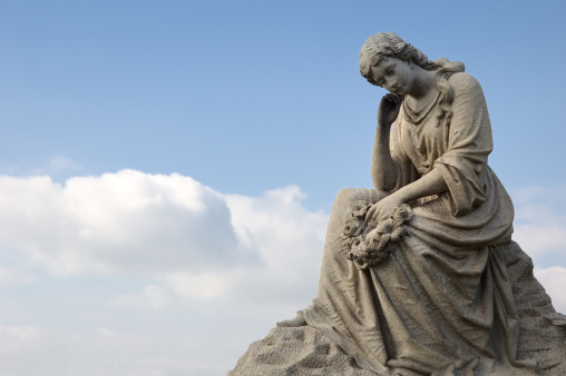 Sad mourning woman with cloud background; a cemetery statue against blue sky.