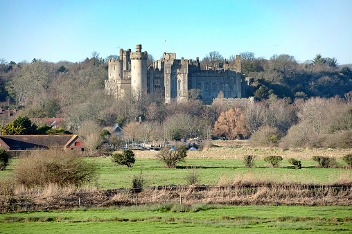 Sun kissed Arundel Castle across water meadows, Arundel, West Sussex, England. Arundel is an ancient market town built at a bridge point over the River Arun, with a skyline dominated by the huge Arundel Castle - built by the Normans - and the Gothic revival architecture of Arundel Cathedral which overlooks the meadows and grasses of the fertile South Downs