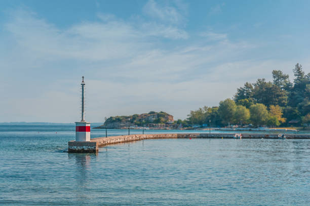 istock Small lighthouse on sea coast with cloudy sky and forest background 1367004375