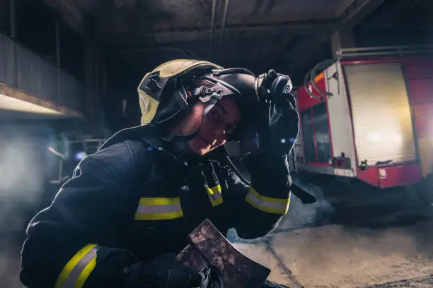 Photo of Portrait of a female firefighter while holding an axe and wearing an oxygen mask indoors surrounded by smoke.