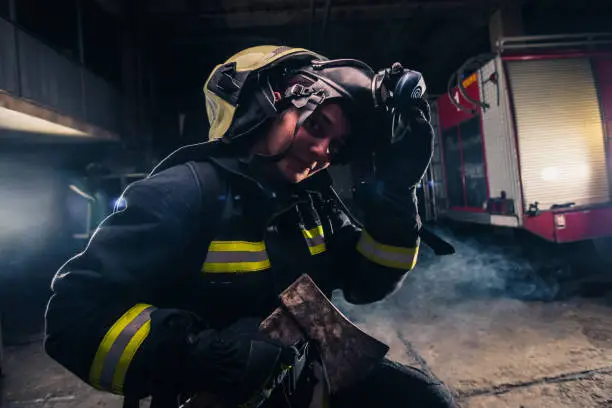 Photo of Portrait of a female firefighter while holding an axe and wearing an oxygen mask indoors surrounded by smoke.