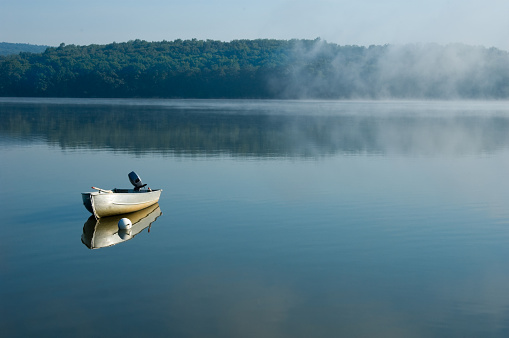 Fishing boat tied on a calm misty morning lake, alone and waiting, Pennsylvania, PA, USA.