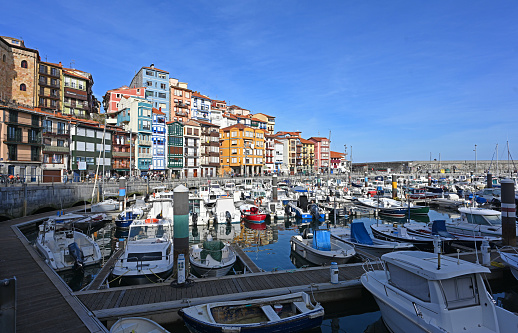 Bermeo, Spain - December 28, 2021: Sail boats are seen on a clear day with colourful houses in the famous old towen and Marina in Bermeo, Spain.