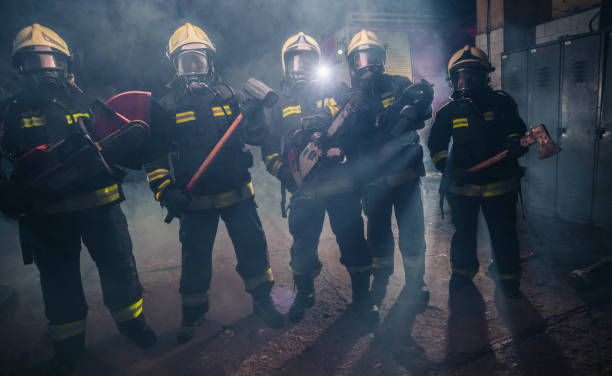 istock Group of firefighters with  chainsaw and sledge hammer practicing in the garage of the fire department 1367008633