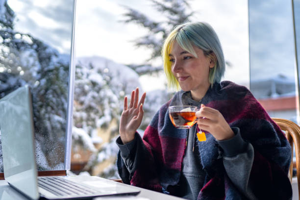 istock Young woman sitting on balcony while snowing and video chatting on laptop while drinking tea 1367010743