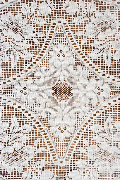 Diamond shape pattern and flowers in an antique lace tablecloth, close-up detail with wood grain background underneath.