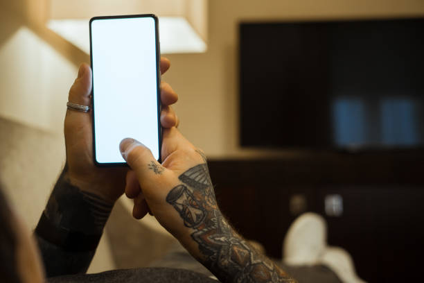 istock Man with tattoos interacting with a phone at night, laying on a couch. 1367015021