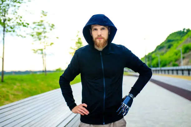 man with arm prosthesis in sports clothing ready for morning workout outdoors. Disabled sport concept.