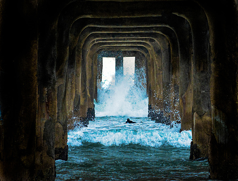 A surfer faces a large wave beneath the pier