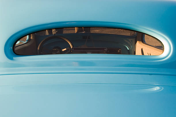 Rear window of a restored baby blue hot rod roadster at a car show, photographed in evening yellow light.