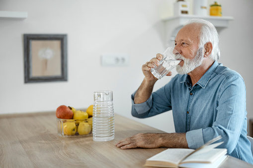Handsome senior man drinking a fresh glass of water in the kitchen