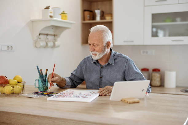 istock Senior man using tablet while painting on canvas at home 1367020957