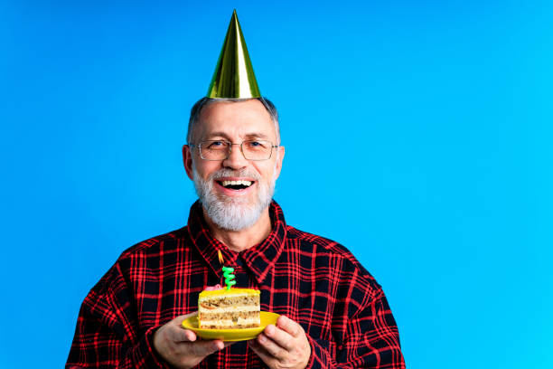 istock man wearing birthday hat with cake isolated on bright blue colour background, studio portrait 1367021125