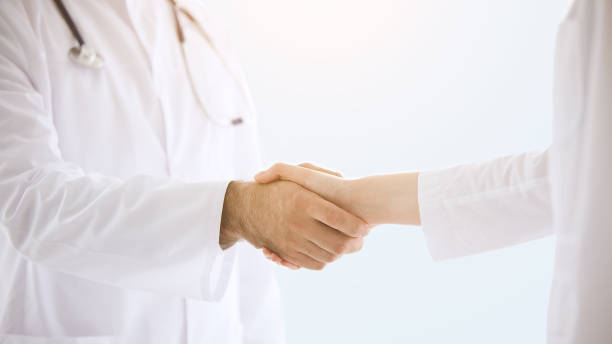 istock Doctors in lab coats greeting each other with handshake isolated over grey color background 1367024291