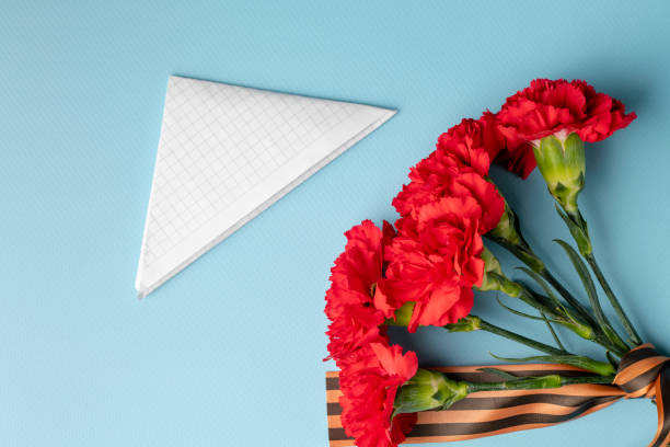 istock a bouquet of red carnations with a St. George ribbon and a triangular military envelope a field mail symbol with space for text on a blue background, top view, holiday background, postcard Defender of the Fatherland Day, May 9 Victory Day 1367026988