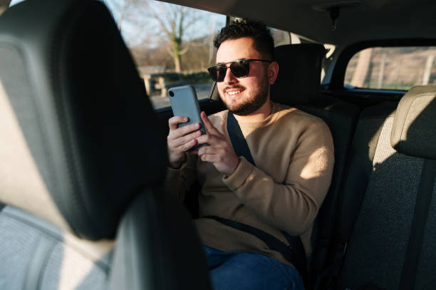 istock Young man using a smartphone while sitting on the back seat of a car 1367028543