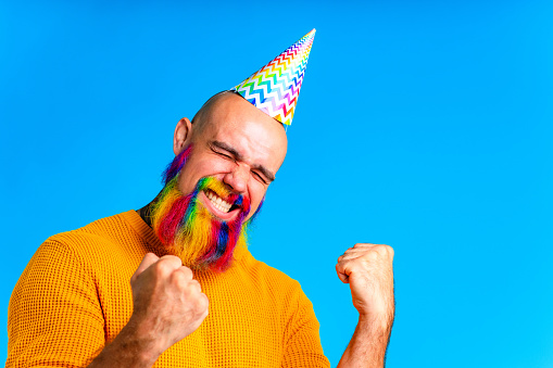 happy man with colorful beard wear horn on head in blue studio background.