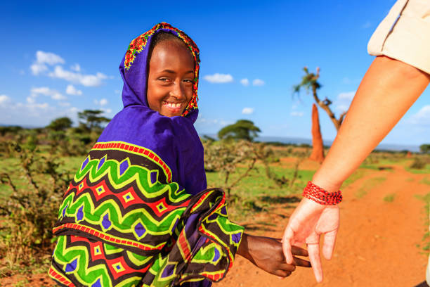 Caucasian female is holding young african child's hand in Ethiopian village.