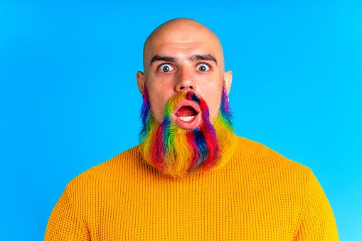 cool man with colorful beard looking at camera and feeling amazing in studio blue background.