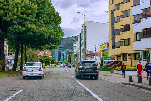 Bogotá, Colombia - October 08, 2021: The drivers point of view on the northbound carriageway of Carrera Novena driving through the Bario de Usaquén in the Andean capital city of Bogota, in South America. There are office and residential buildings on either side of the road. In the far background are the Andes Mountains. The altitude at street level is 8660 feet above mean sea level. Horizontal format. Copy space.