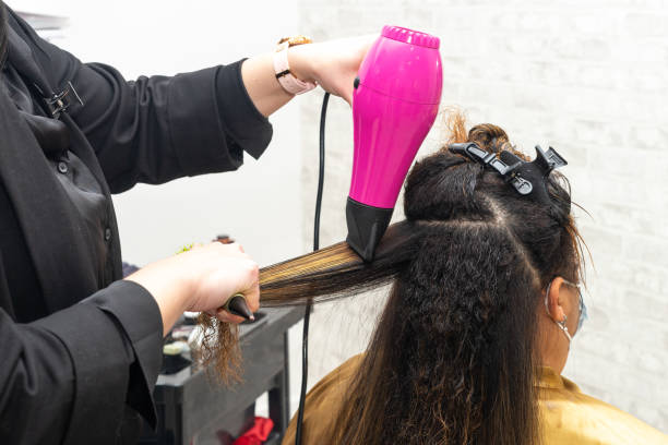 Hairdresser drying the hair of a client with damaged hair in a beauty salon using a hairdryer and a round brush. stock photo