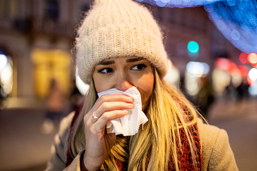 Woman with Cold or Flu is Blowing her Nose on a street