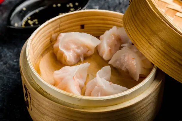 Dim sum with shrimp on wooden plate on dark stone table macro close up