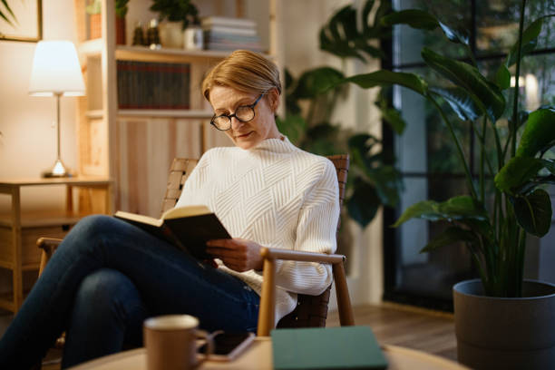 istock Mature woman reading book at home 1367042878