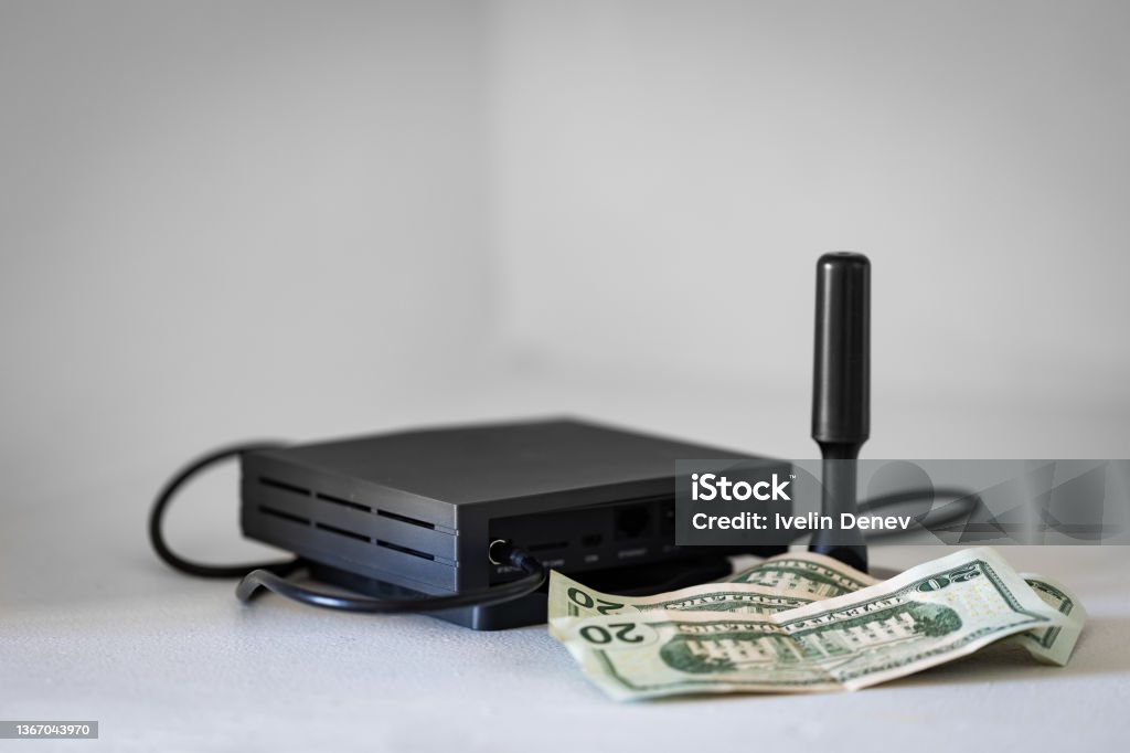 Dollar bills in front of radio communication device HNT cryptocurrency miner hotspot with antenna for radio connection and dollar bills as an association with profits from blockchain mining Helium Stock Photo