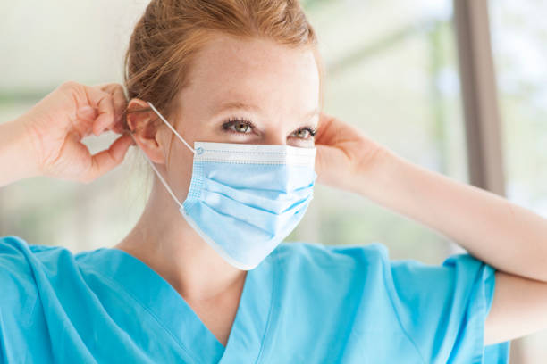 Beautiful young redhead woman nurse in scrubs wearing medical pandemic face mask covering stock photo