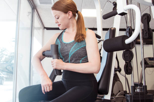 istock Young beautiful redhead woman using massage gun on arm in gym 1367048595
