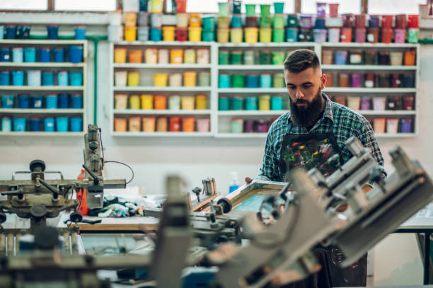 männlicher arbeiter mit druckmaschine in einer werkstatt - silk screen fotos stock-fotos und bilder