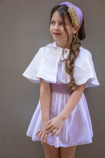 Little Caucasian girl, preteenager, posing in her white and violet ceremony dress and cape, looking so cute and chic.