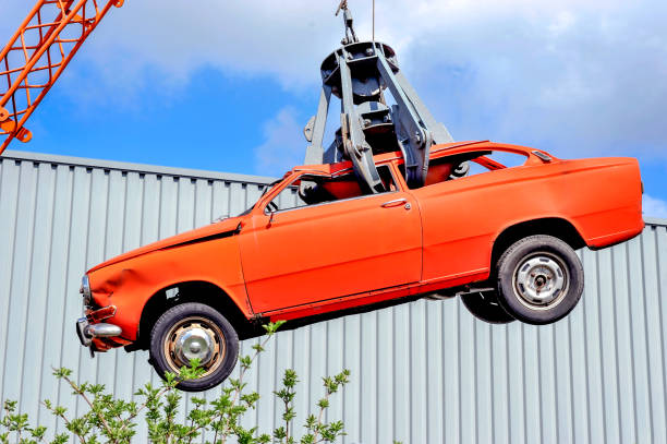 épave de voiture ancienne rouge sur le crochet dans une décharge prête pour la presse à ferraille suspendue dans les airs avec un ciel bleu - casse automobile photos et images de collection