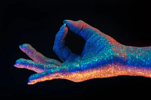 Jnana Gian mudra - Om on black background. Female hand covered with holographic shining glitter under neon colored. High quality photo