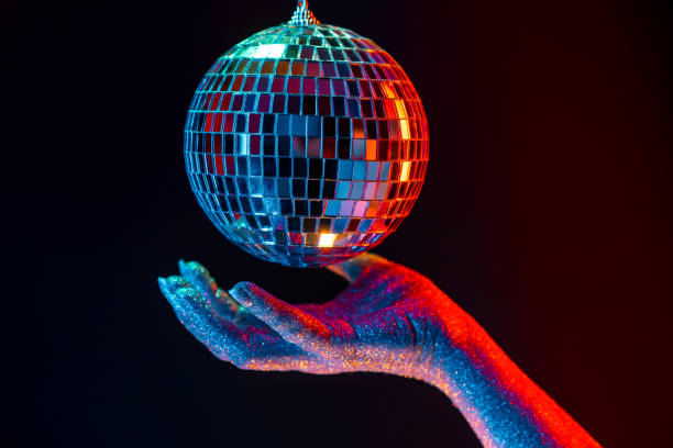 istock Glitter female hand holding spinning disco mirror ball under neon. Glossy silver sphere reflecting light. Retro night party, music and entertainment concept background 1367056007