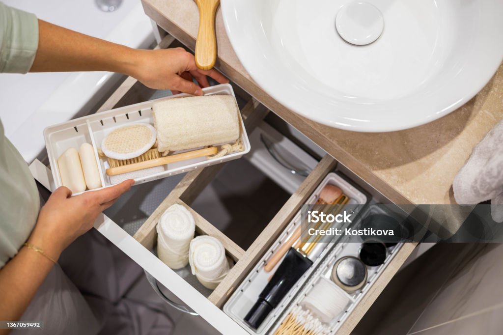Top view of woman hands neatly organizing bathroom amenities and toiletries in drawer in bathroom Top view of woman hands neatly organizing bathroom amenities and toiletries in drawer or cupboard in bathroom. Concept of tidying up a bathroom storage by using Marie Kondo's method. Bathroom Stock Photo