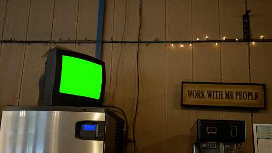 A Green Screen TV Sitting On Top of Fridge In Restaurant or Coffee Bar