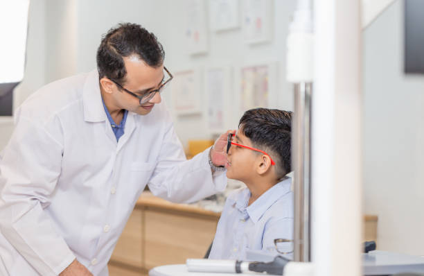 istock Boy doing eye test checking examination with optometrist in optical shop, Indian child choosing eyeglasses in optics store, Optometrist doing sight testing for child patient in clinic 1367069615