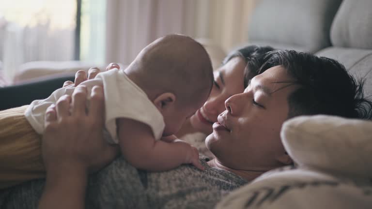 Asian Chinese parent lying down bonding with their baby boy on bed in weekend morning together