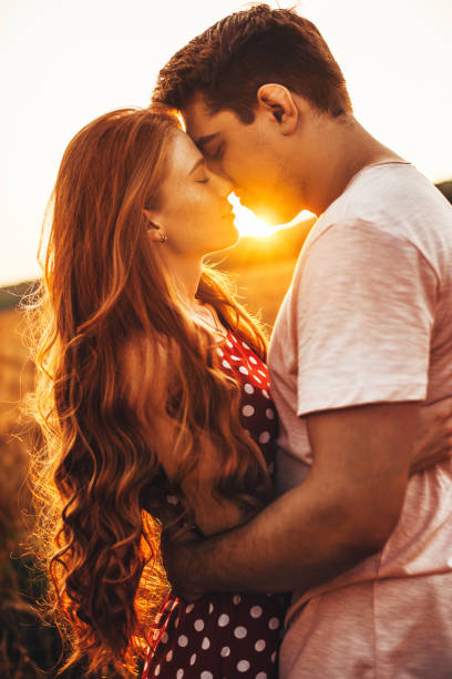 vista laterale di una donna con lunghi capelli rossi che bacia il marito a una riunione all'aperto. posare sullo sfondo luminoso - couple passion women love foto e immagini stock