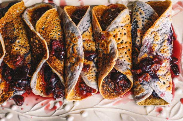 Pancakes baked with cherry juice and pieces, filled with fresh cherry compote and rolled