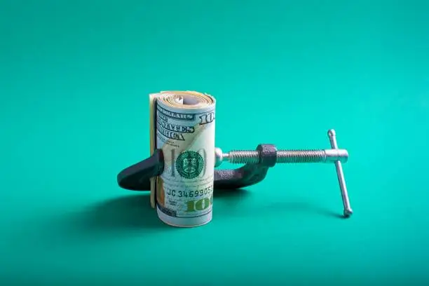 Photo of Clamp squeezing roll of U.S. 100 dollar bills