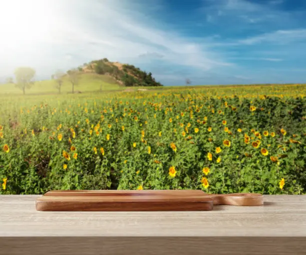 Wooden cuttingboard on wooden table for standing product against sunflower field