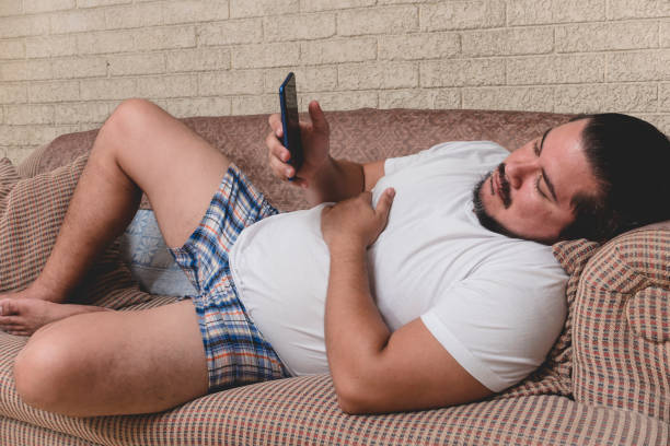 ein müder und gelangweilter slacker in boxershorts ist während eines faulen tages auf der couch süchtig am telefon. - hotel reception stock-fotos und bilder