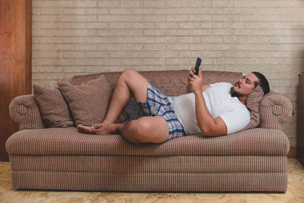 An jobless and lazy man browses his social media or the internet all day while lying on the couch An jobless and lazy man browses his social media or the internet all day while lying on the couch asian inactivity stock pictures, royalty-free photos & images