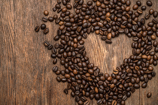 Heart shape made by roasted roasted coffee beans on a wooden background, directly above.