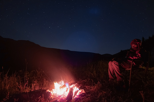Woman is resting near fireplace at night time with night sky background.