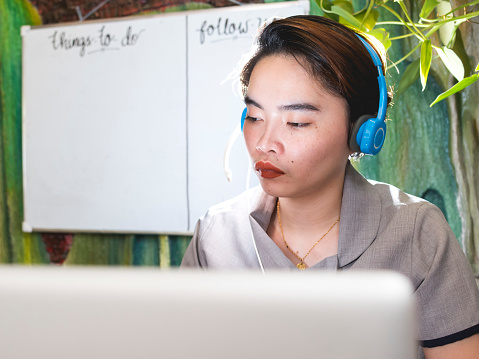 A filipina woman in work uniform but at home engaged at transcribing, listening to audio on her headset.