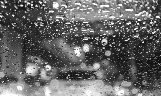 Closeup of raindrops on the car windshield with blurry street at night in monochrome